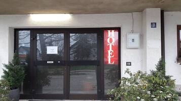 L’entrée d’un hôtel, avec une porte en verre et une enseigne rouge indiquant le nom de l’hôtel.