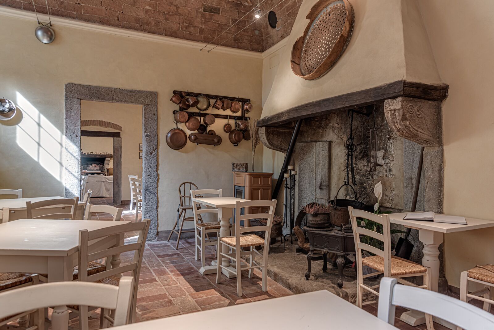 Un comedor rústico con mesas y sillas blancas, pared de ladrillo y un colgador para ollas.