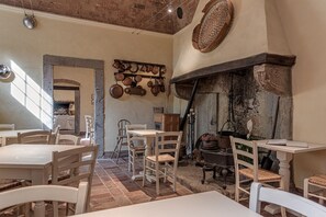 Un comedor rústico con mesas y sillas blancas, pared de ladrillo y un colgador para ollas.