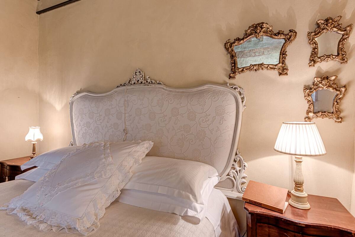 Ein Schlafzimmer mit einem großen, verzierten Bett, zwei Nachttischen und drei Wandspiegeln.