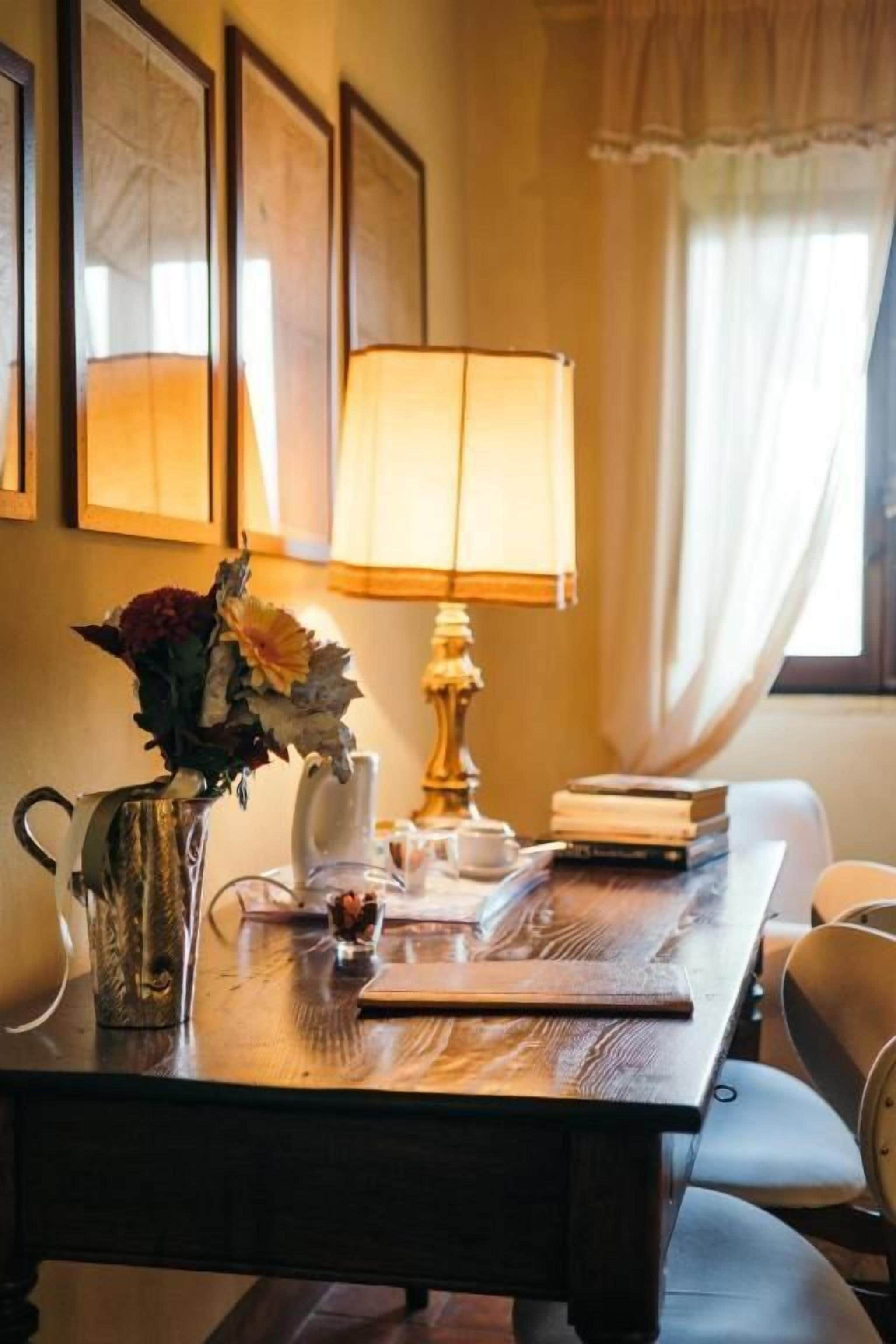 A wooden table with a lamp, a vase with flowers, and a pitcher.