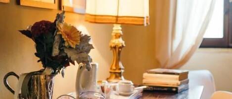 A wooden table with a lamp, a vase with flowers, and a pitcher.