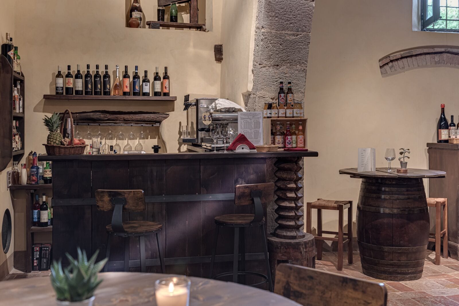 Un rústico espacio de bar con muebles de madera, una pared de piedra y estantes llenos de botellas de vino.