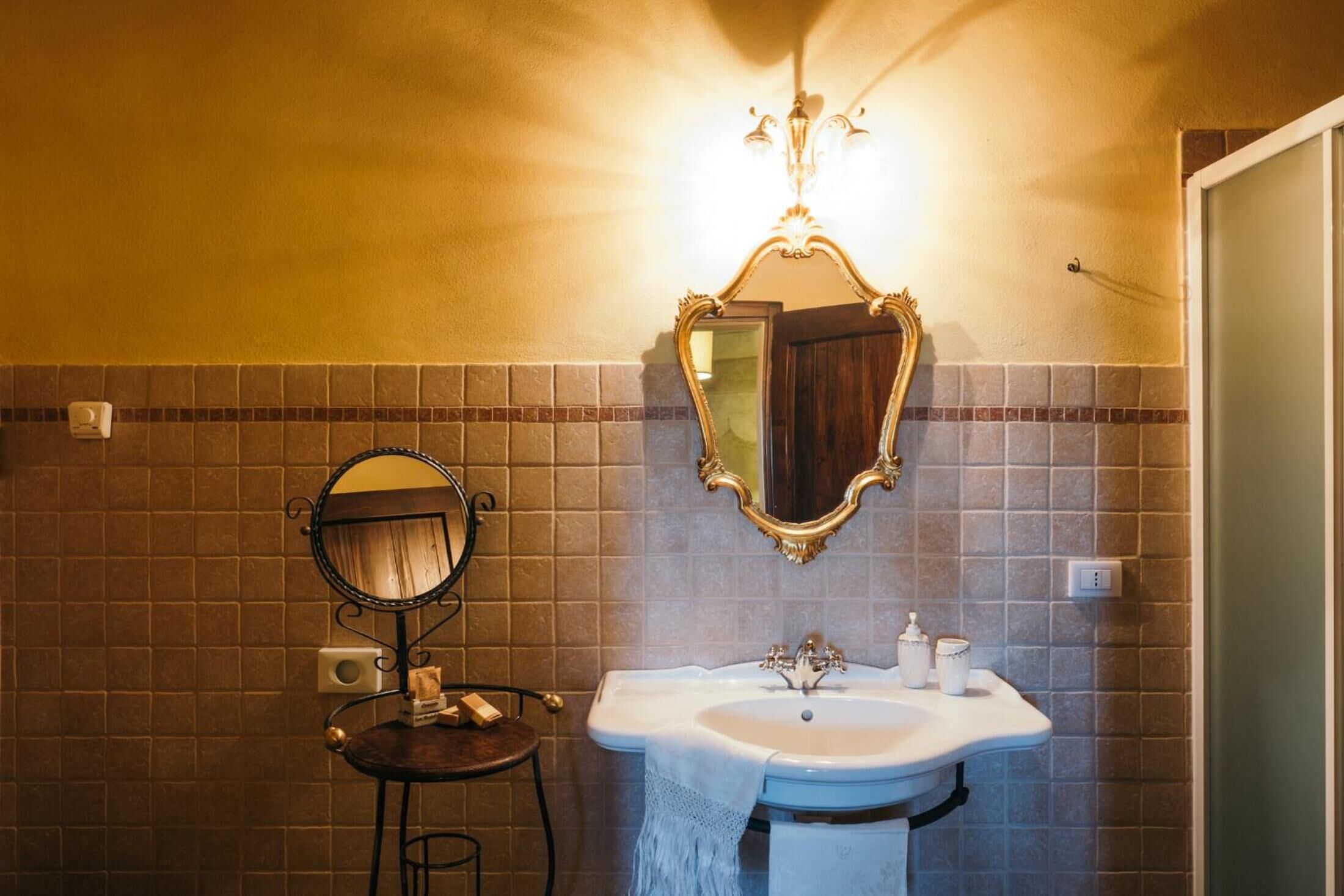 Un baño con un lavamanos, dos espejos y una lámpara fijada a la pared.