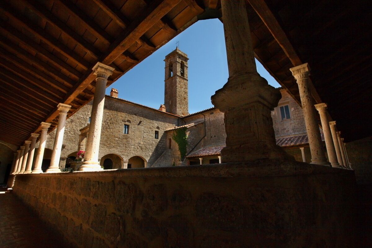 A courtyard with stone columns, a stone building, and a tower in the background.