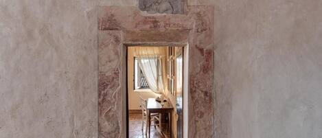 A corridor with a stone wall, a framed portrait, and a table with chairs.