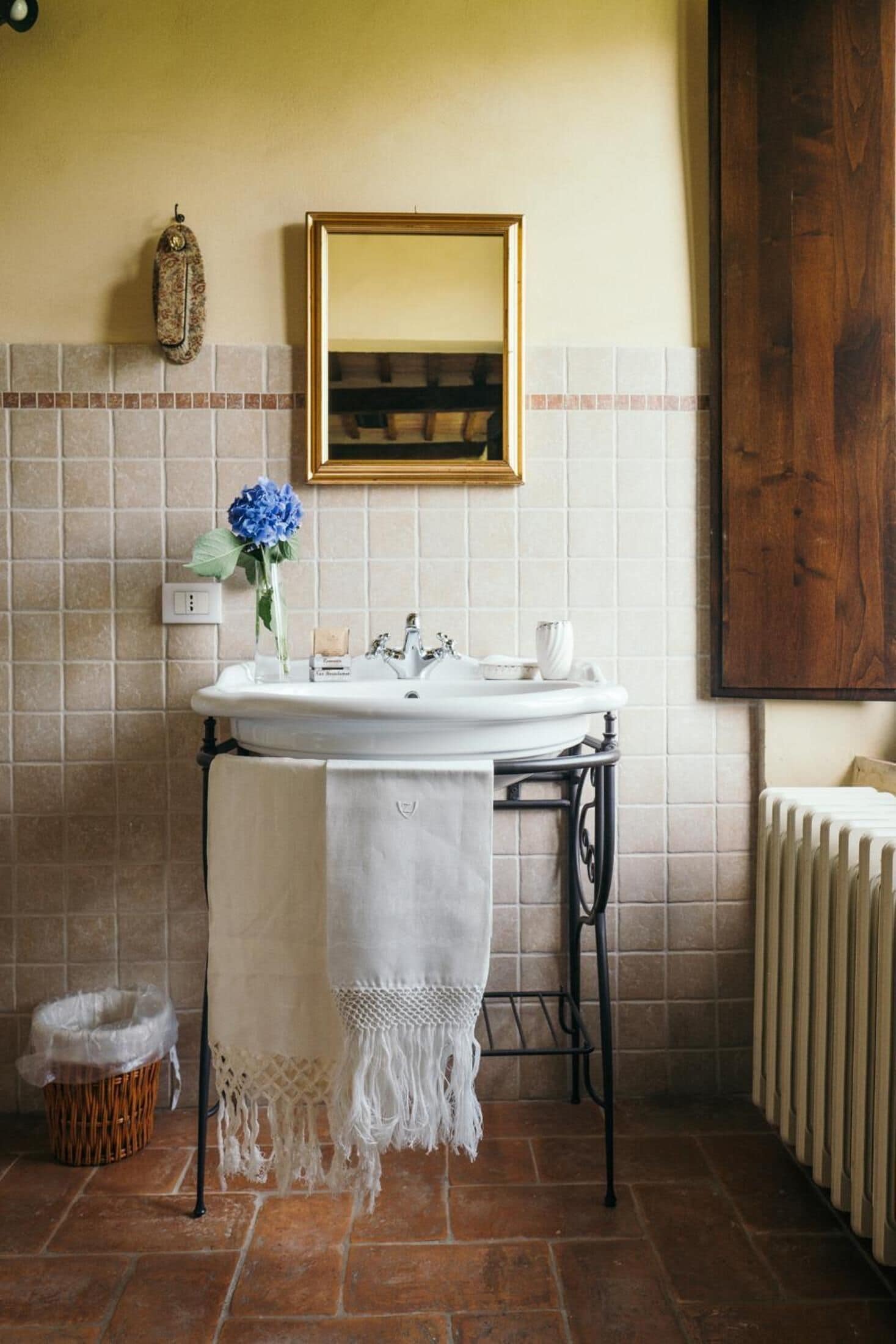 A bathroom with a white sink, a towel draped over the edge, a blue flower vase, and a wooden cabinet.