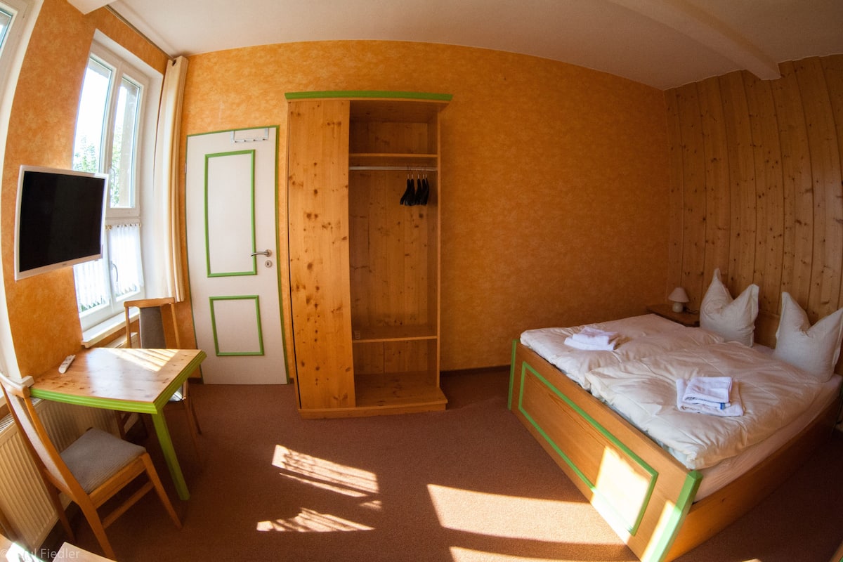 A room with a bed, a desk, a chair, a wardrobe, and a television.