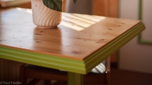 Una planta en maceta con flores moradas sobre una mesa de madera con detalle verde.