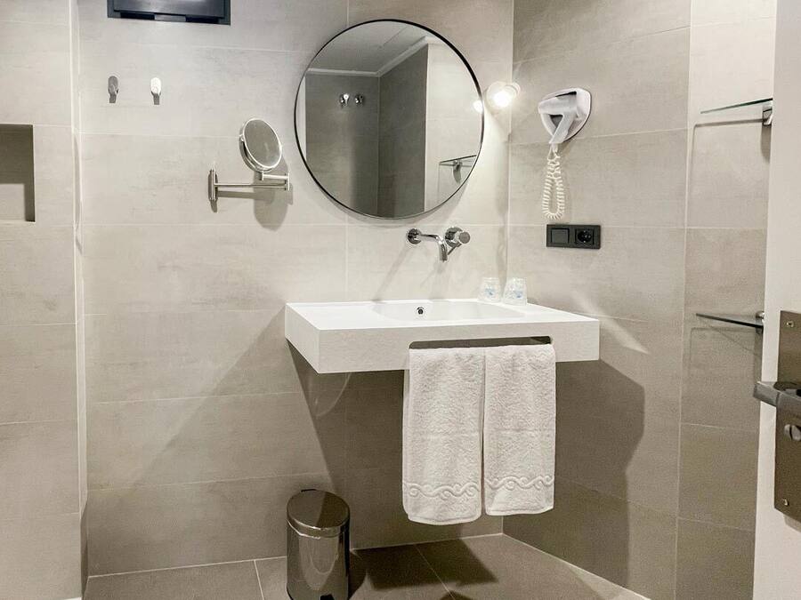 A modern bathroom with a rectangular sink, a round mirror, a handheld showerhead, and a toilet.