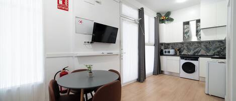 Eine moderne Küche mit Waschmaschine, einem Essbereich inklusive Tisch und Stühlen sowie einem Wand-Fernseher.