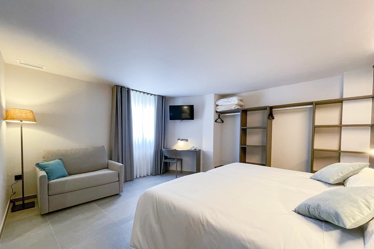Ein Hotelzimmer mit Bett, Schreibtisch, Stuhl, Sofa und Fernseher.
