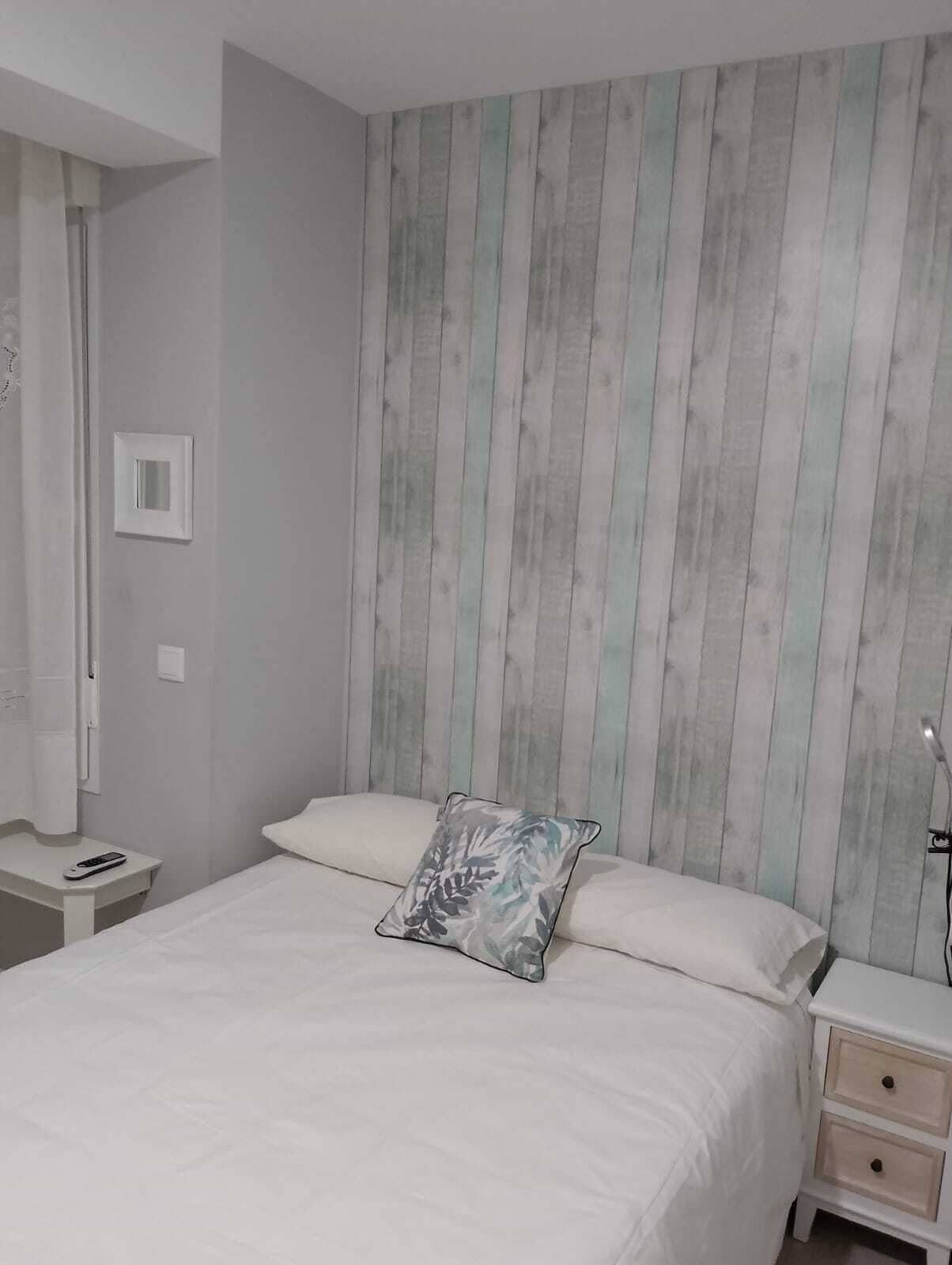 A bedroom with a bed, a nightstand, a bedside table, and a wall with vertical stripes.