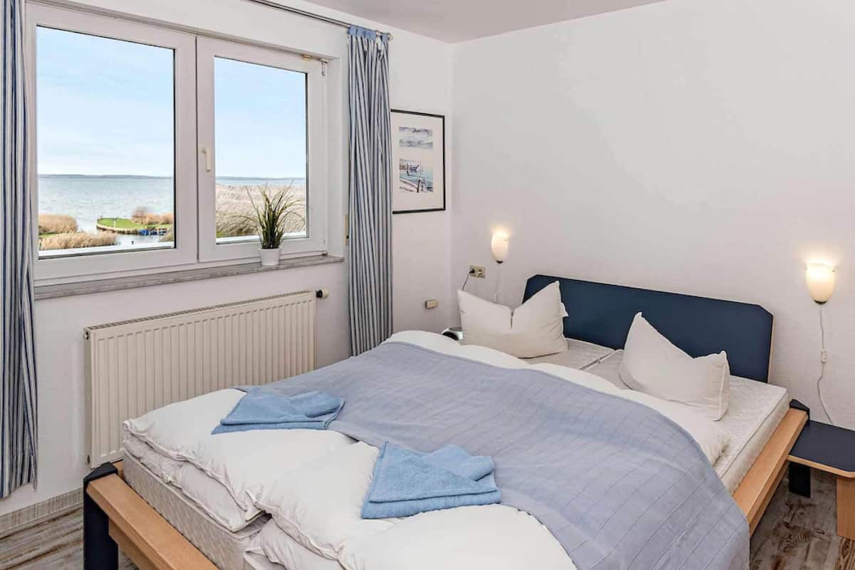Ein Schlafzimmer mit einem Bett, einem Fenster mit Vorhängen, einem Nachttisch und einer Wandleuchte.