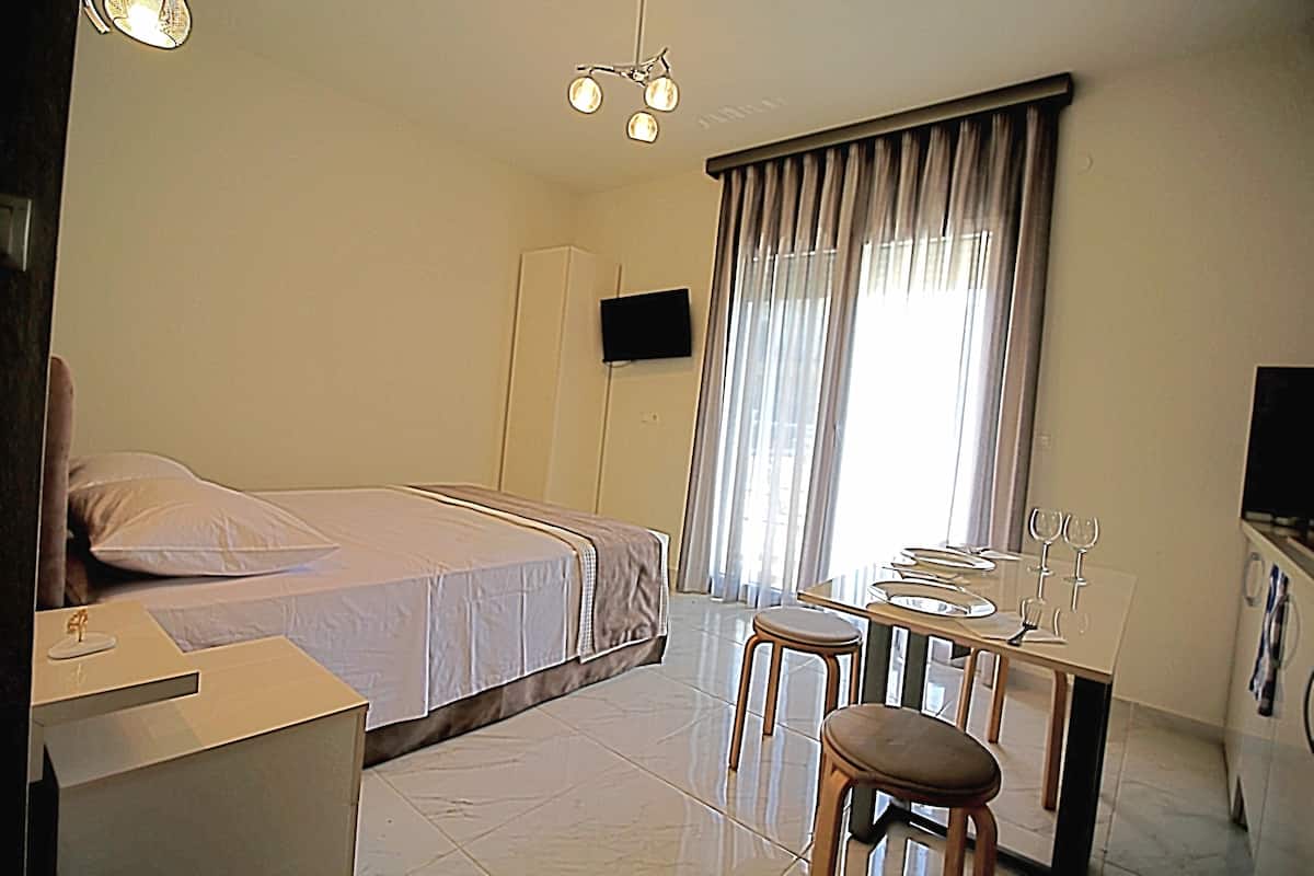 A hotel room with a bed, a desk with two chairs, a flat-screen TV mounted on the wall, and a window with curtains.
