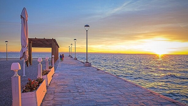 Un molo in pietra che si protende in uno specchio d'acqua, con un tramonto sullo sfondo.