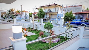 Zona residenziale con un giardino curato, un balcone con ringhiera e un'auto blu parcheggiata sulla strada.
