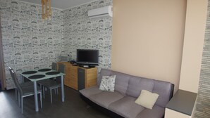 En hyggelig opholdsstue med sofa, spisebord med stole, fjernsyn og tapet med mønster.