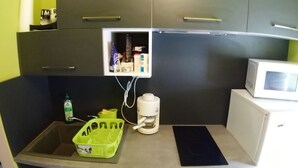 Et lille tekøkken med mikrobølgeovn, kaffemaskine og et skab med diverse ting.