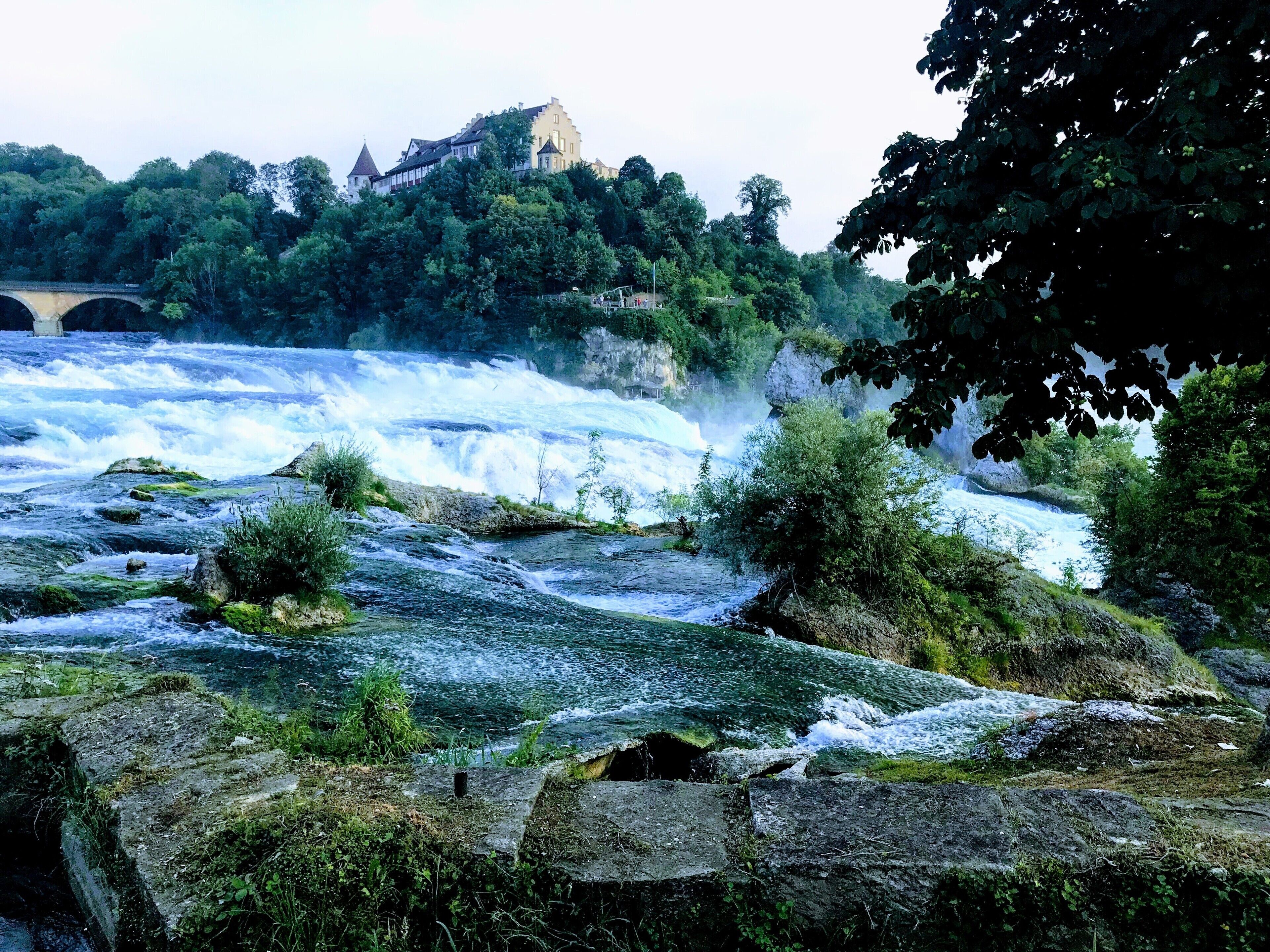 A river with a waterfall and a bridge in the background.