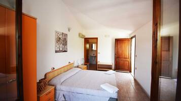 Une chambre à coucher avec un lit, une table de chevet, une armoire en bois, une salle de bain visible à travers une porte ouverte et un luminaire fixé au mur.