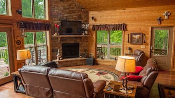 L’intérieur chaleureux d’un chalet avec une cheminée, des meubles en cuir et de grandes fenêtres donnant sur le paysage extérieur.