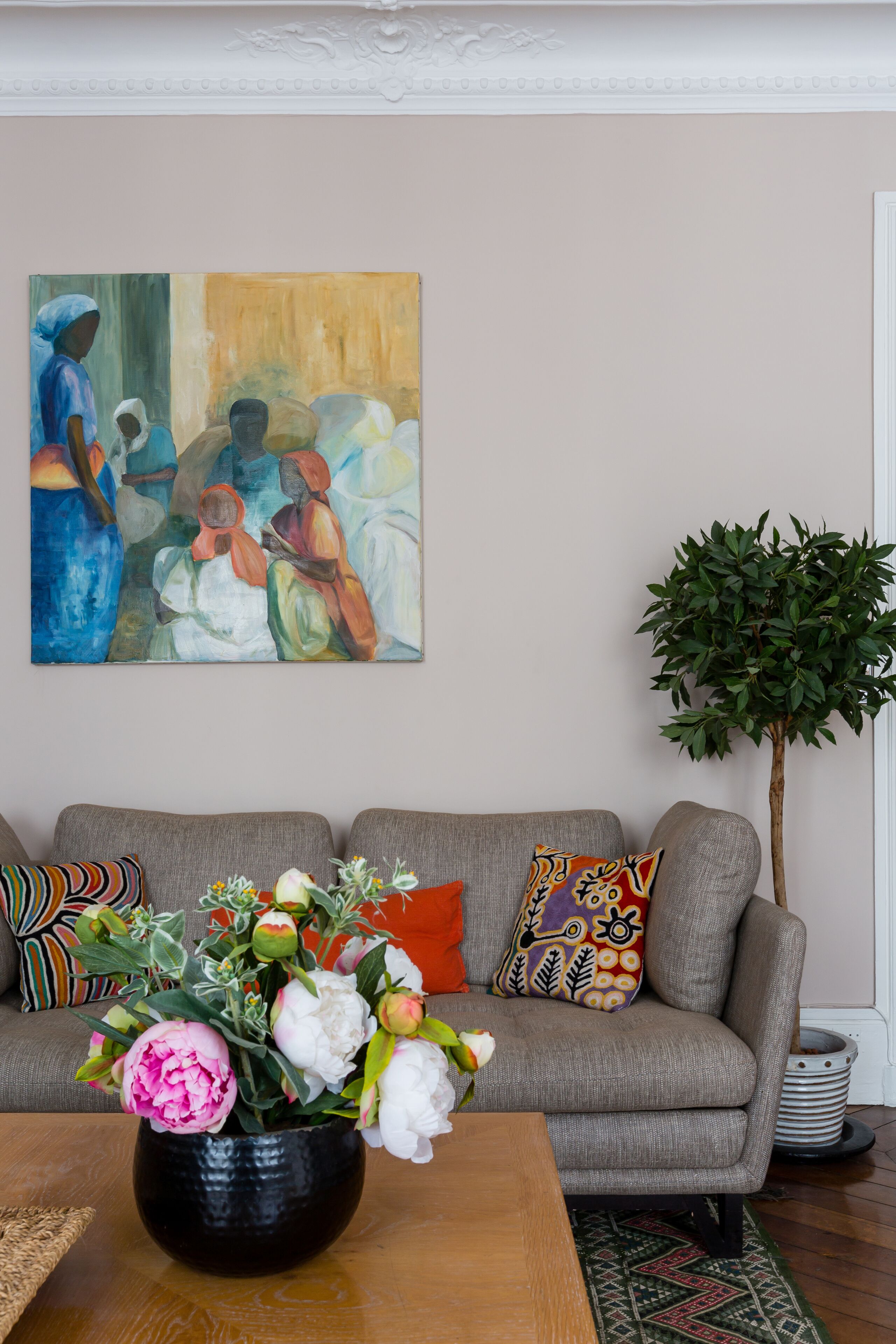 A living room with a grey sofa, colorful pillows, a vase of flowers, and a painting on the wall.