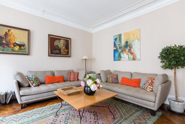 A living room with a grey sofa, colorful cushions, a wooden coffee table, and a potted plant. - Muted Beauty in Batignolles, by Veeve (Paris)