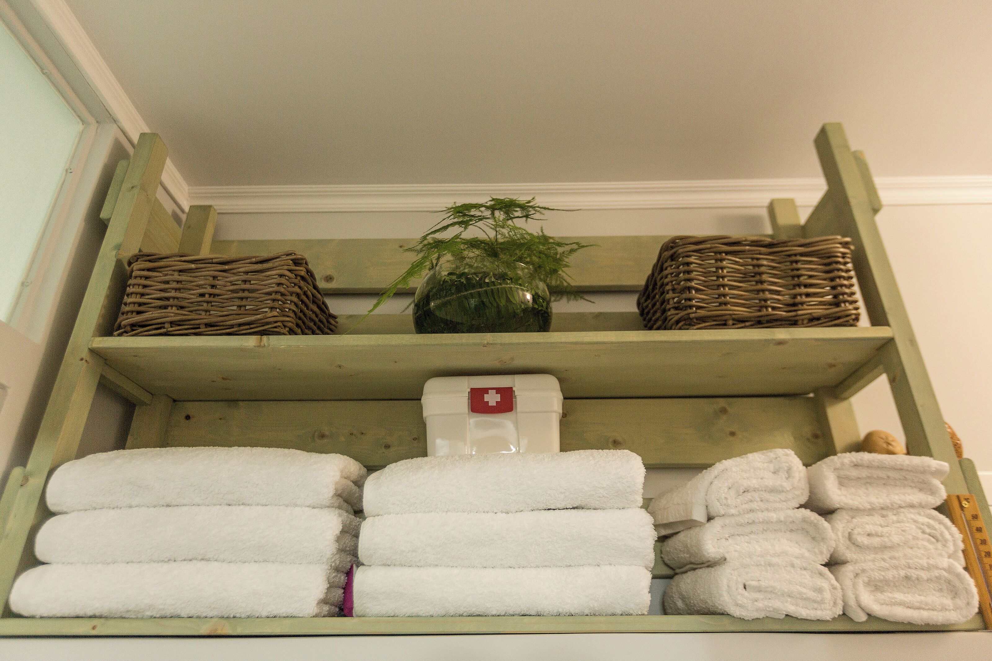 A shelf with folded white towels, a wicker basket, and a potted plant.