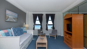 A room with a bed, a sofa, two chairs, a small table, a TV stand, and two windows with curtains. - 625 Ocean View Hollywood (Hollywood)