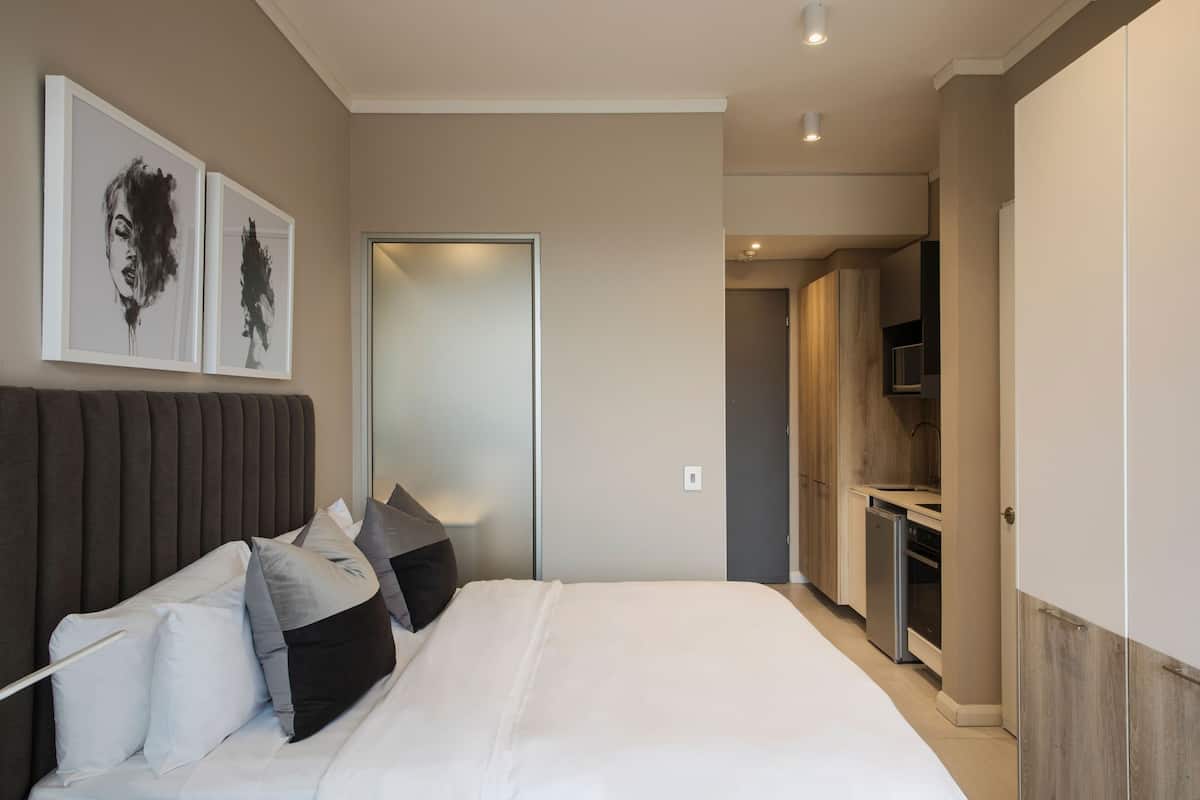 A modern bedroom with a large bed, a wardrobe, and a bathroom visible through an open door.