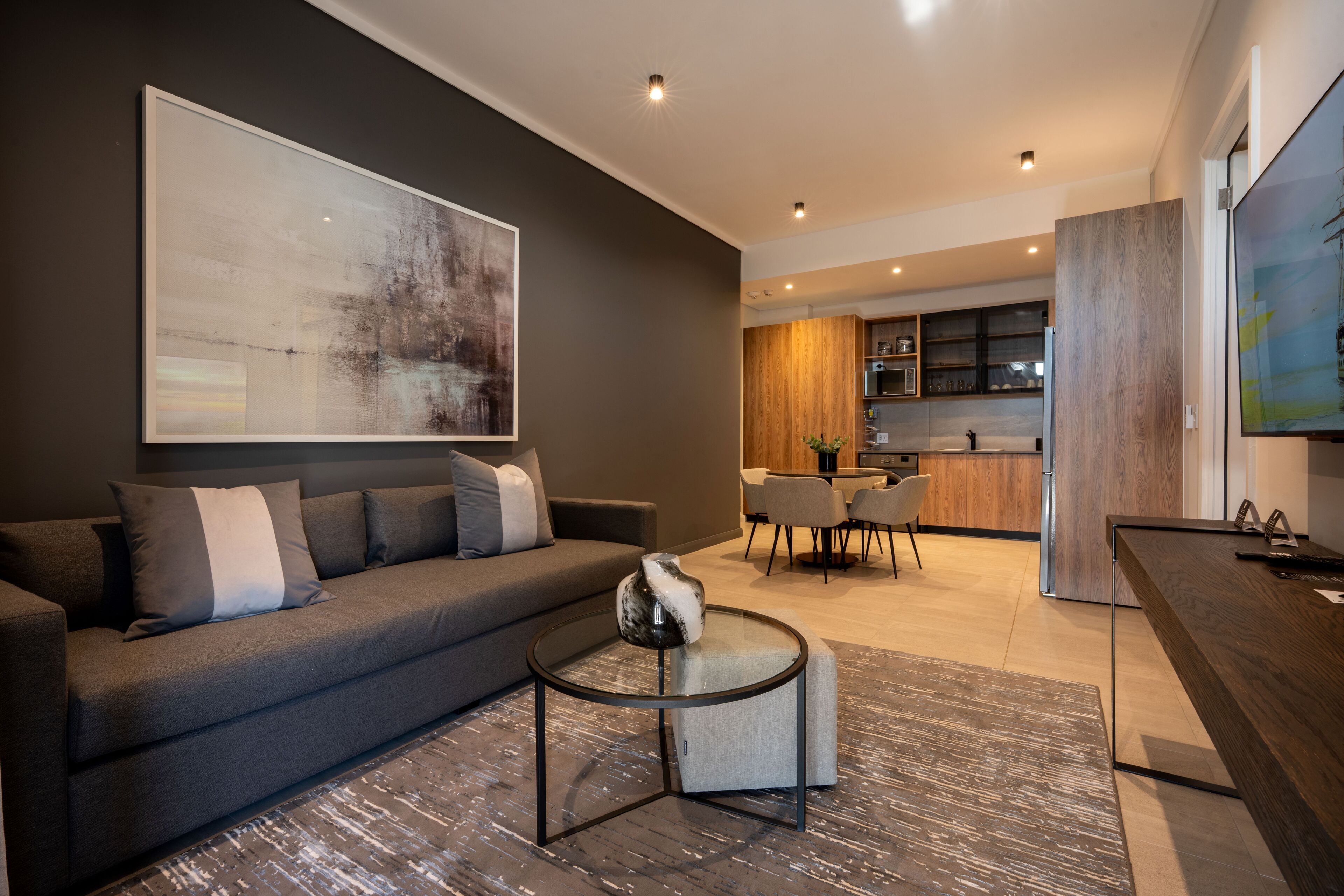 Una sala de estar moderna con un sofá gris, una mesa de centro redonda y un cuadro abstracto grande.