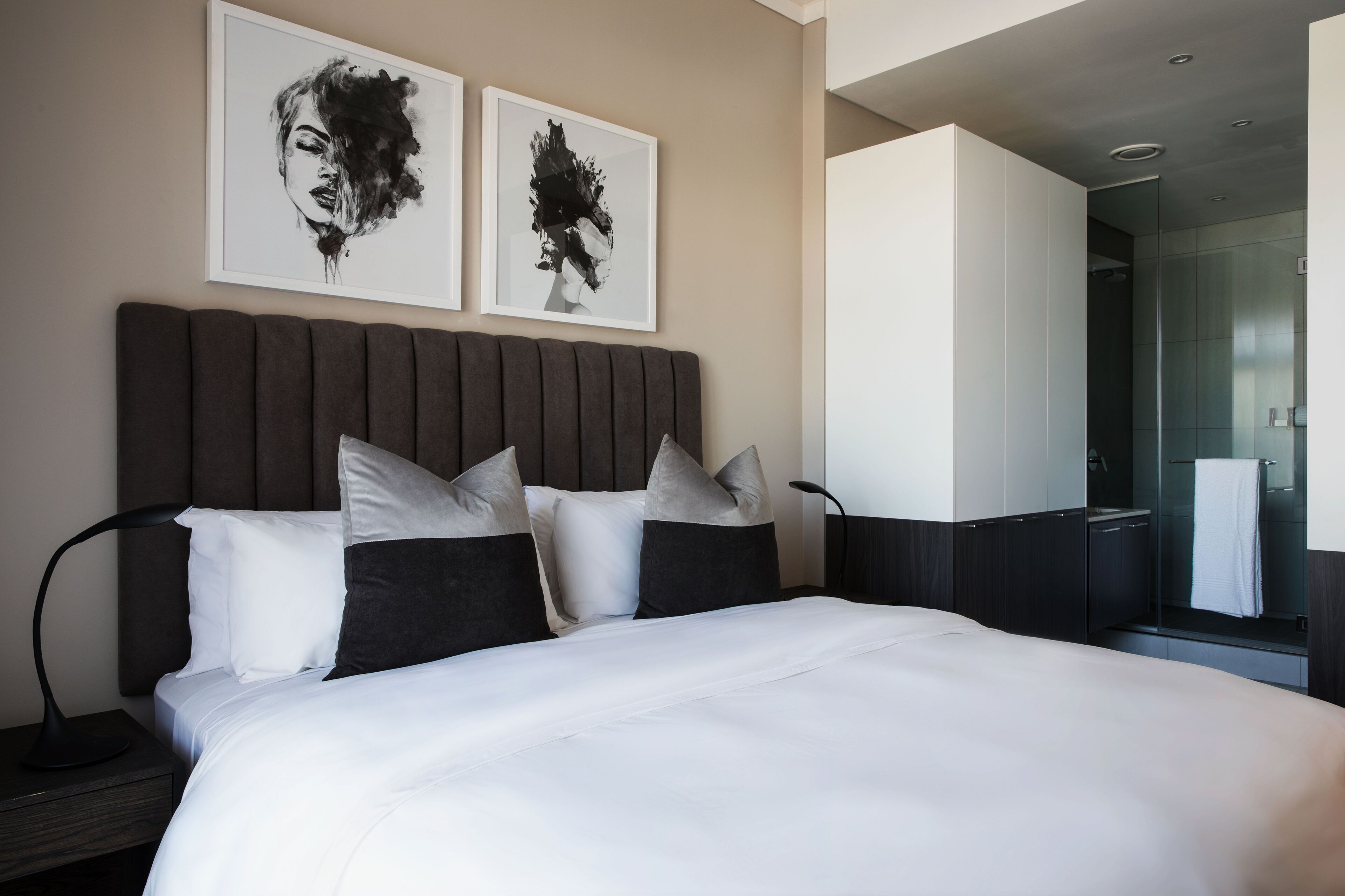 Een moderne hotelkamer met een groot bed, twee ingelijste kunstwerken aan de muur en een zichtbare badkamer.