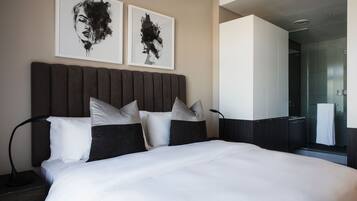 Een moderne hotelkamer met een groot bed, twee ingelijste kunstwerken aan de muur en een zichtbare badkamer.