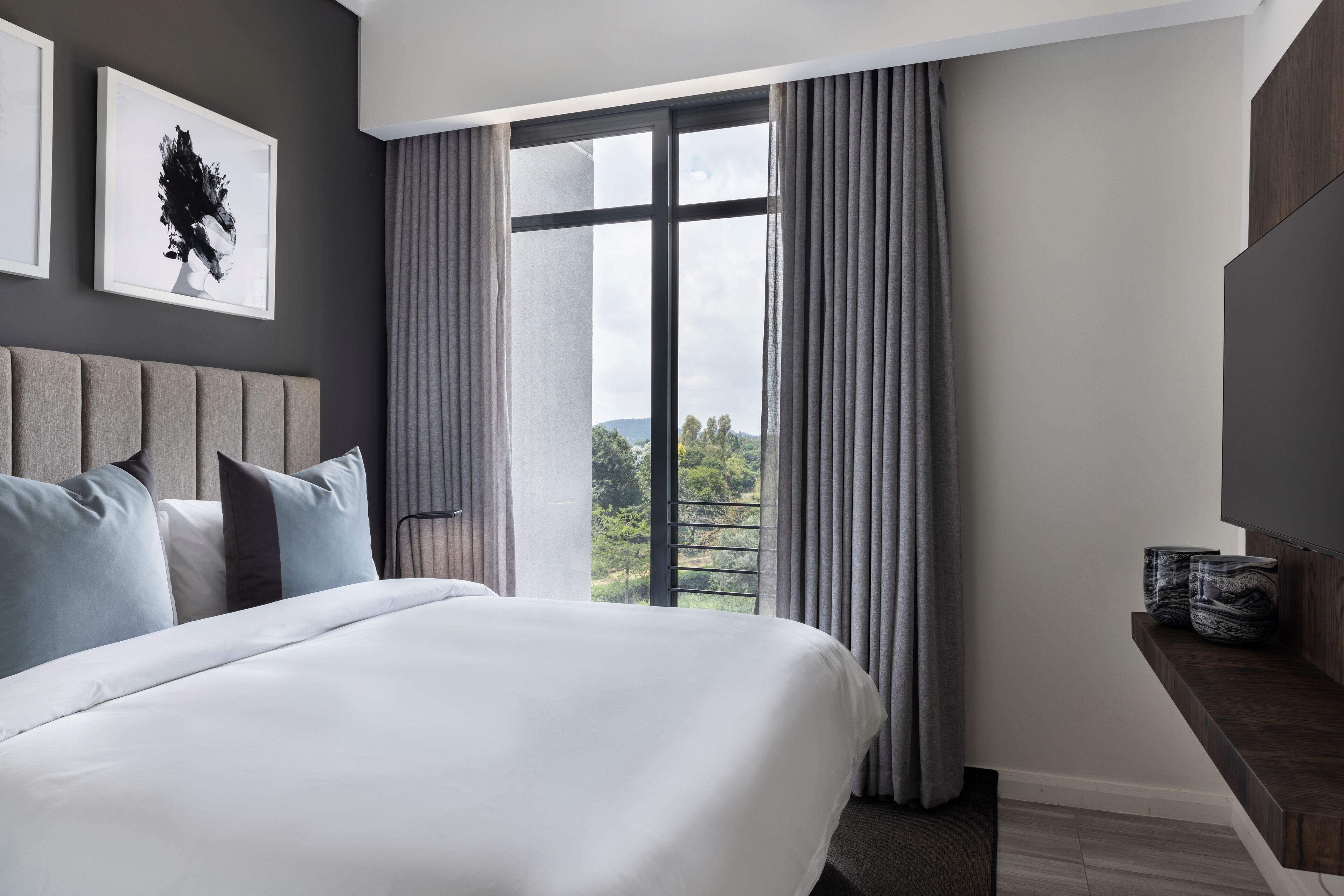 Habitación de hotel moderna con una cama grande, vista a zonas verdes por una ventana y una obra de arte colgada en la pared.