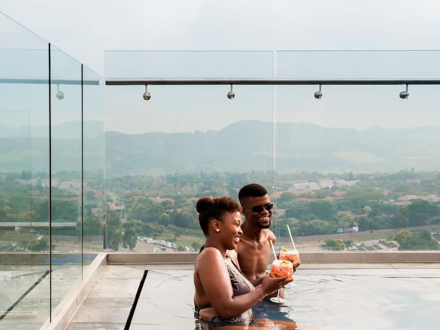 Ein Paar sitzt an einem spiegelnden Infinity-Pool mit Blick auf die Stadt.