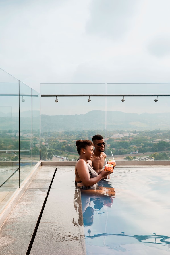 Una pareja sentada junto a una piscina infinita que refleja una vista panorámica de la ciudad.