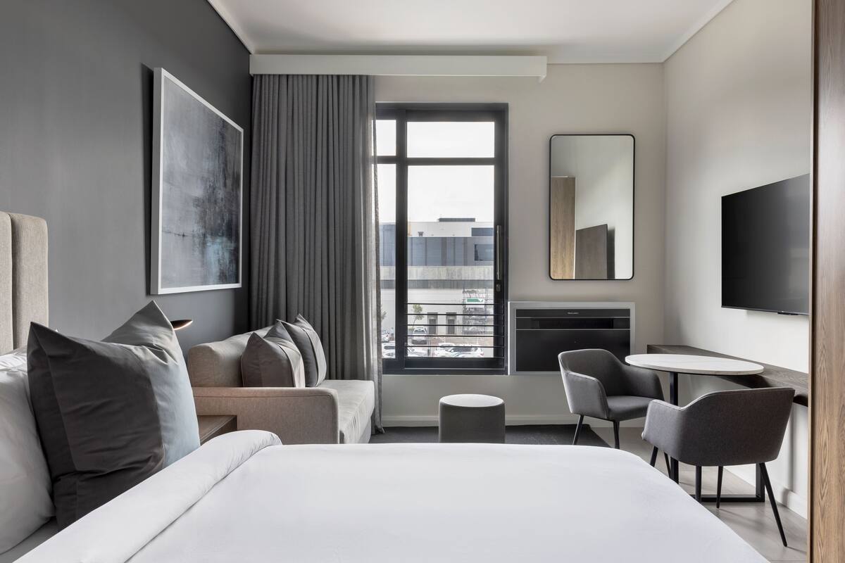 A modern hotel room with a large bed, a sofa, a dining table, and a TV.