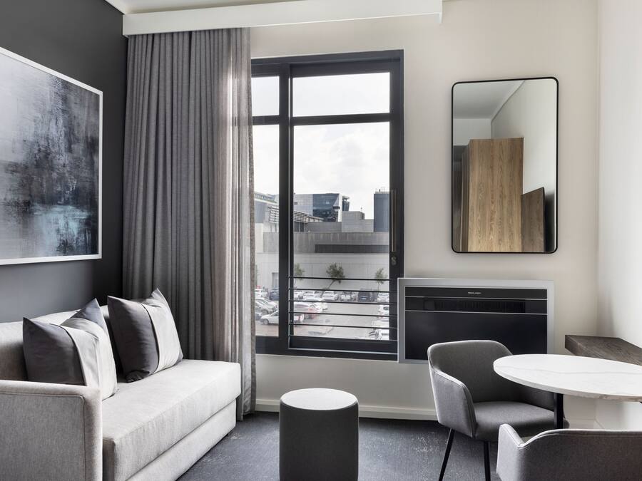 Una habitación de hotel moderna con un sofá gris, una mesa redonda y un ventanal con vista a la ciudad.