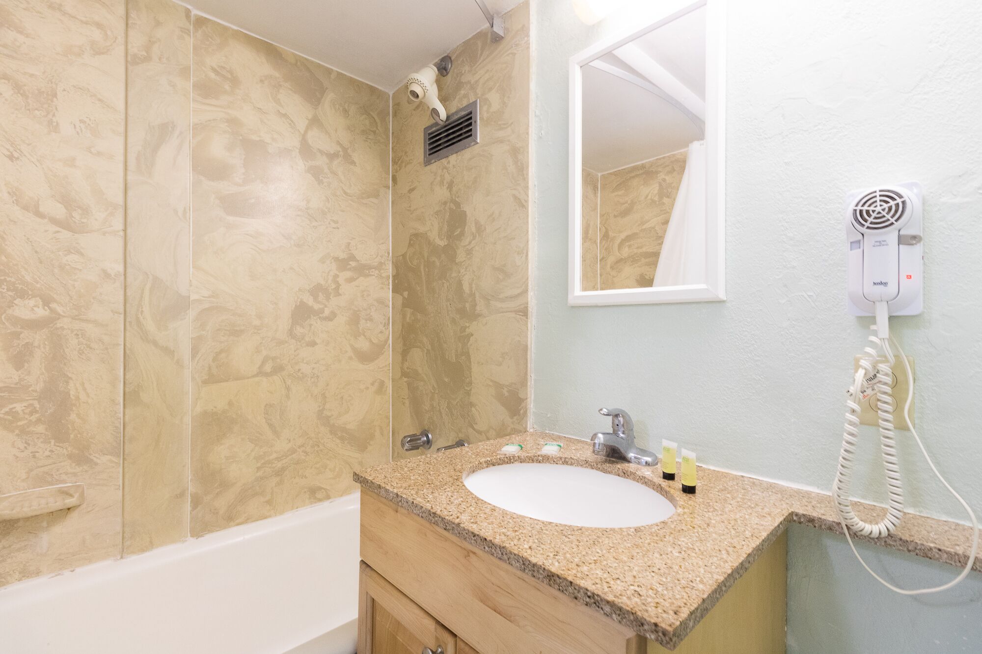 A bathroom with a marble wall, a sink with a granite countertop, a mirror, a hairdryer, and a telephone.