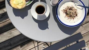 Ett runt bord med en tallrik mat, två koppar kaffe och en skål med yoghurt och olika tillbehör.