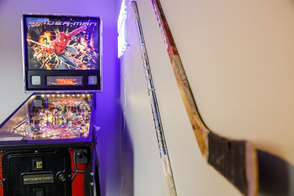 A pinball machine with a Spider-Man theme, a broom leaning against a wall, and a poster on the wall. - Hotell Nyboholm (Ulricehamn)