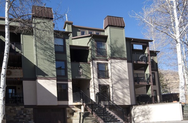 Un edificio residencial de varios pisos con base de piedra, revestimiento verde y varios balcones.