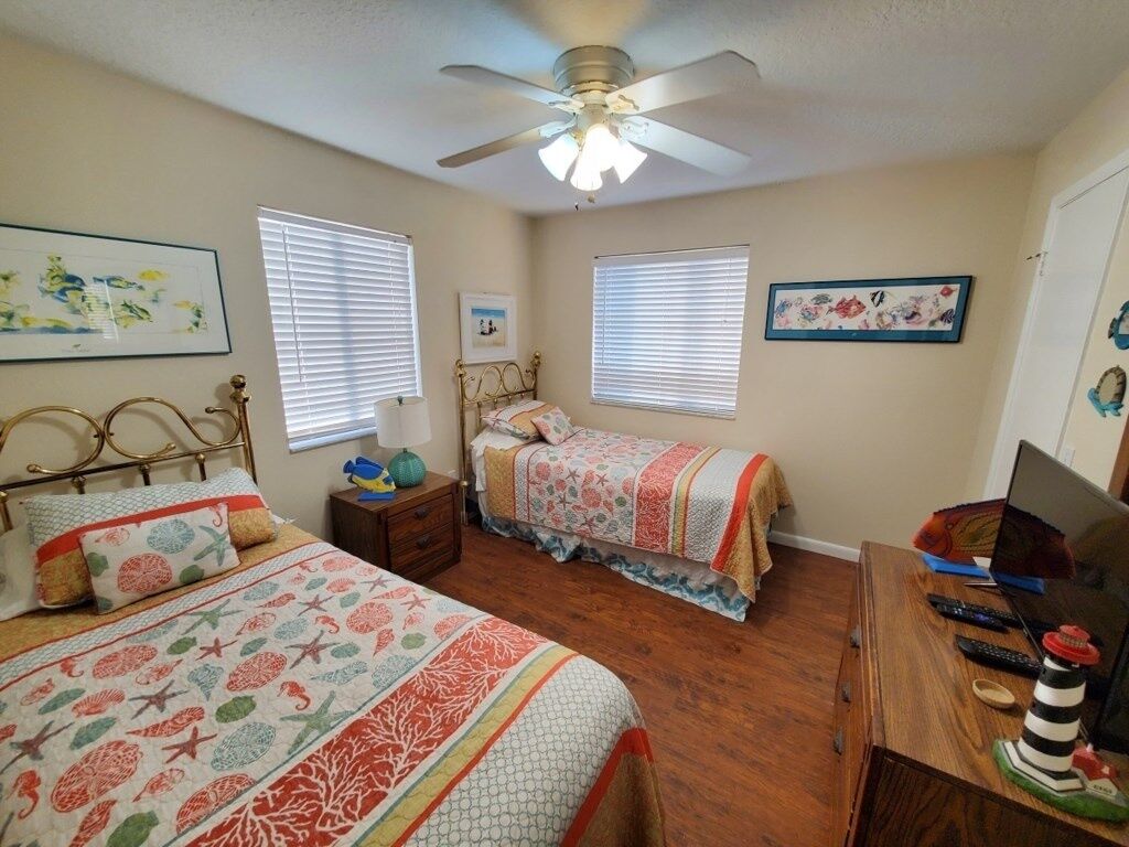 A bedroom with two beds, a ceiling fan, a desk with a computer, and a window with blinds.
