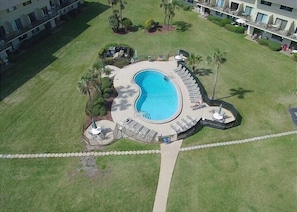 Vista aérea de un hotel con una piscina central rodeada de sillas de descanso y palmeras.