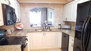 A kitchen with white cabinets, a granite countertop, a stainless steel refrigerator, a microwave, and a dishwasher. - Surf Club I, 1405 2 Bedroom Condo by RedAwning (Palm Coast)