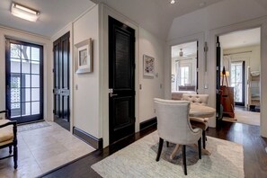 Un hall d’entrée spacieux avec une porte sombre, un coin repas avec une table ronde et des chaises, et une vue sur le salon attenant.