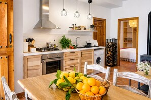 A modern kitchen with wooden cabinetry, a dining table with a fruit basket, and a laundry area.