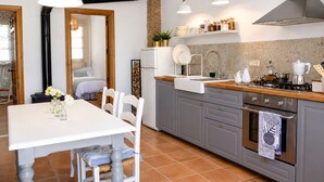 Eine moderne Küche mit grauen Schränken, einer weißen Arbeitsplatte und einem eingebauten Ofen. Es gibt eine Essecke mit weißem Tisch und Stühlen sowie eine Kücheninsel mit Spüle und Herd.
