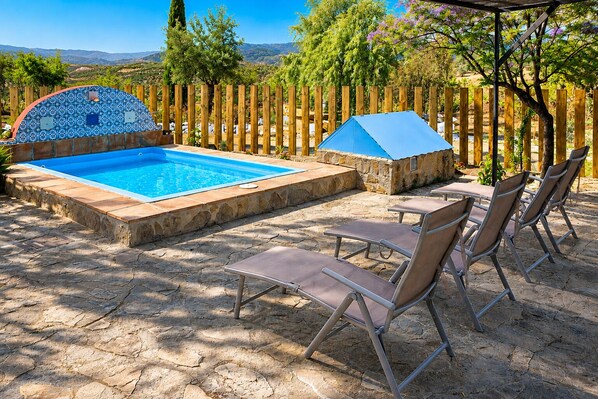 A swimming pool with a tiled deck, lounge chairs, and a wooden fence.